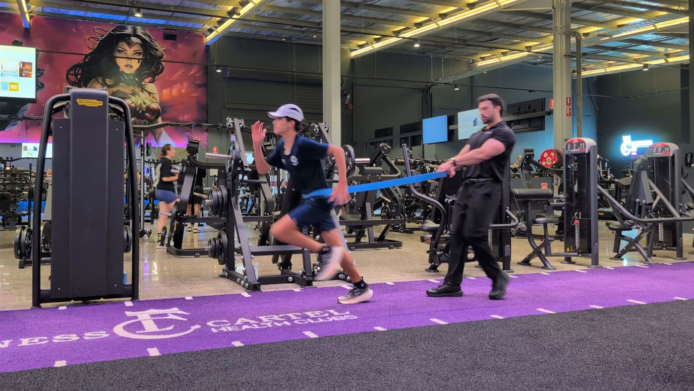 A SYSTM performance coach guiding a young athlete through resistance-band sprint training